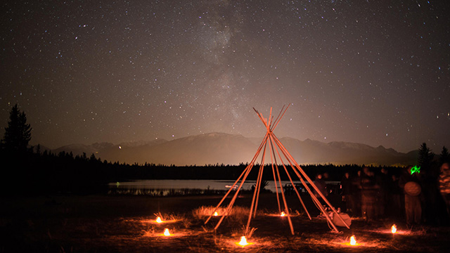 Pôles de tipi avec un éclairage au sol sous le ciel nocturne.