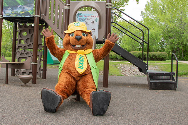 Une mascotte de castor est assise au bout d’une glissade, les mains en l’air.