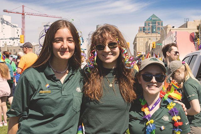 Three Parks Canada summer students smile at the camera at the Pride Winnipeg parade in downtown Winnipeg.