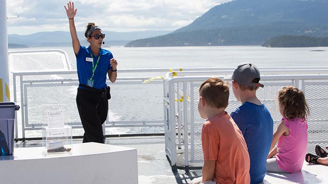An employee with BC Ferries speaks with three children.