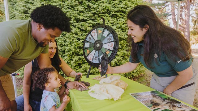 A Parks Canada Outreach team member showing a bear paw replica to a family of three people at a pop-up booth.