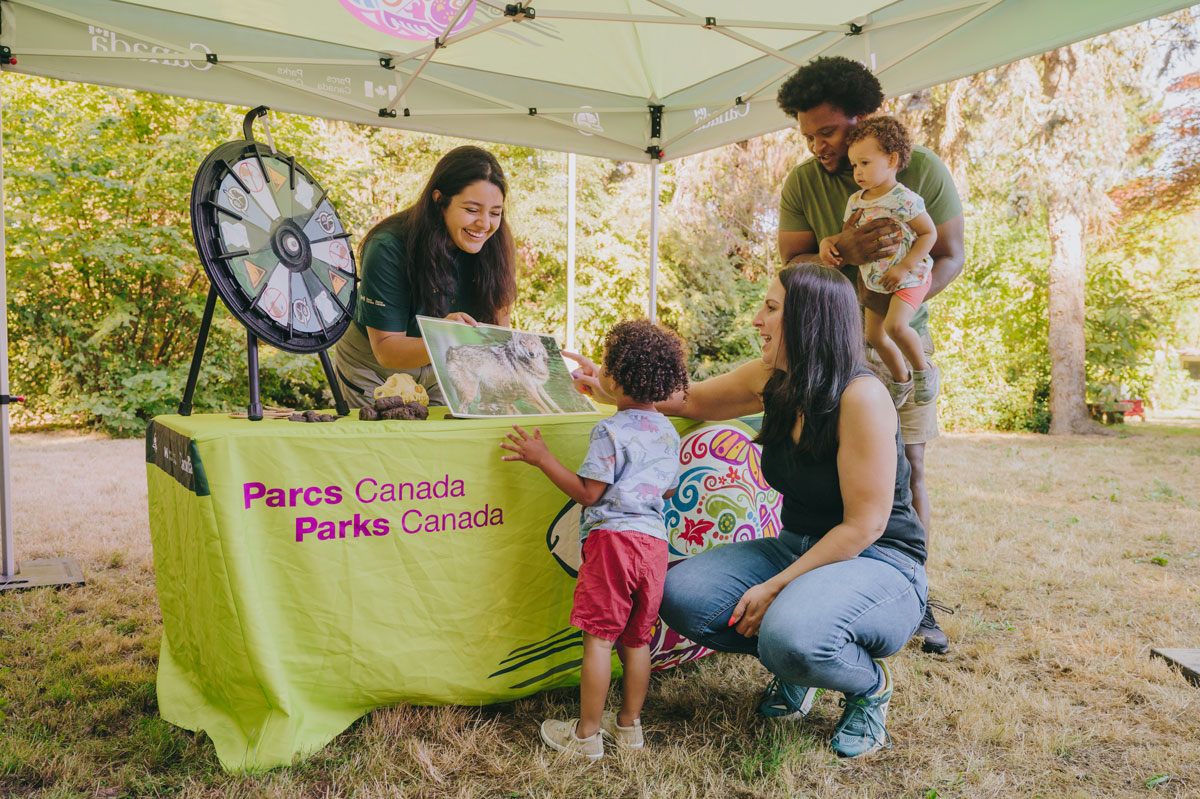 A Parks Canada staff member showing a photo of a wolf to a family of four at a pop-up outreach booth.