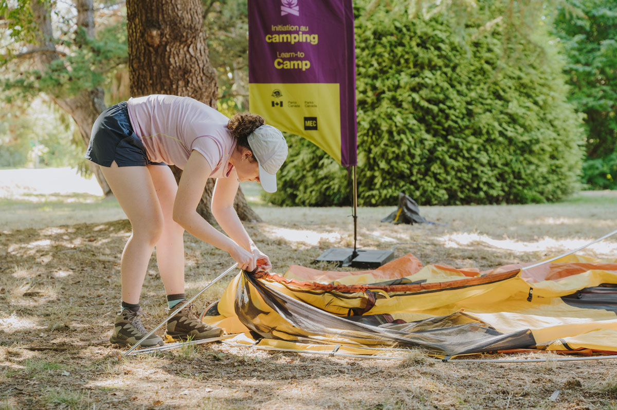 A person setting up a tent with a Learn-to Camp flag in the background. 