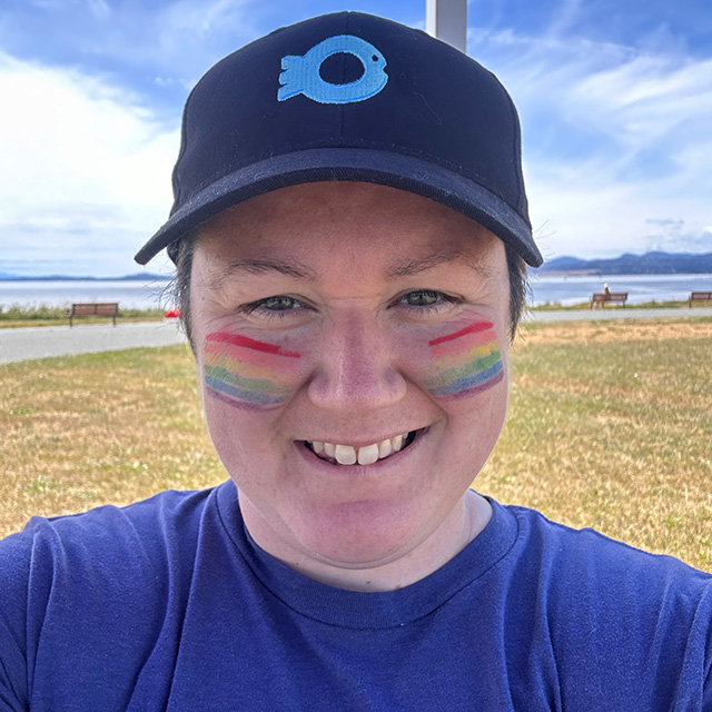 Image of Dr. Chloe Robinson wearing a hat with the Ocean Wise symbol and rainbows in front of a beach.