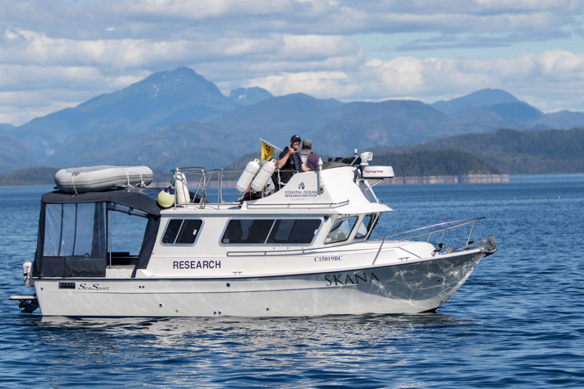 Gary sur le bateau de recherche de Ocean Wise nommé Skana. Il y a des montagnes en arrière-plan.