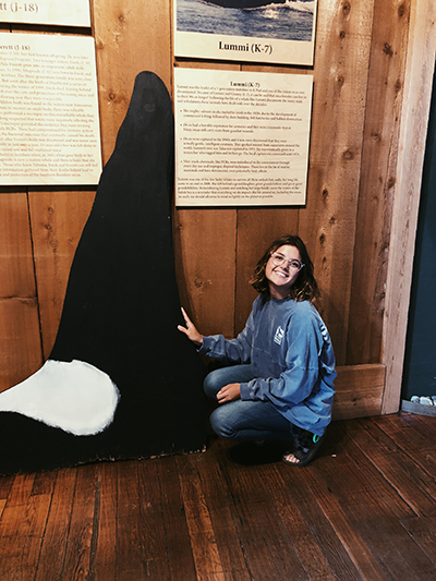 Kendy kneeling beside a life-size replica of a killer whale dorsal fin