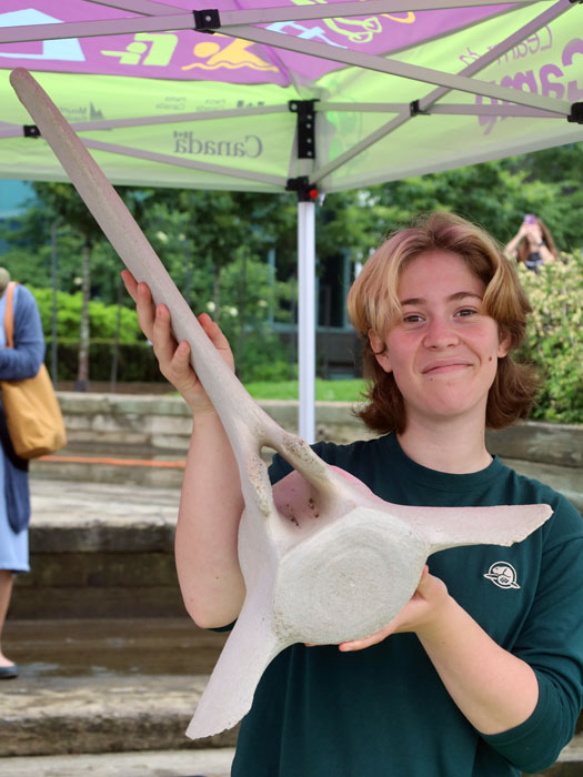 Learn-to camp holding a giant whale bone at an outdoor booth.