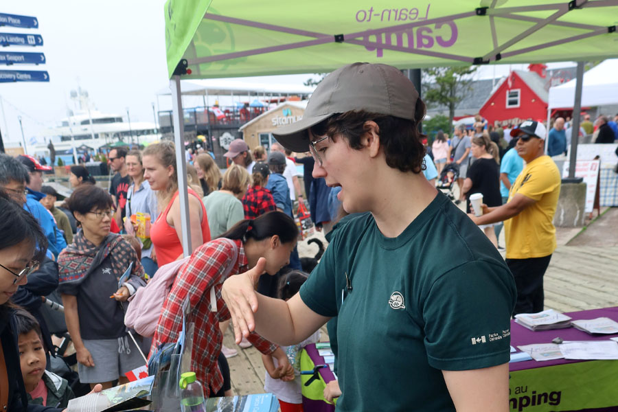 Learn-to camp staff talking to visitors at an outdoor booth.