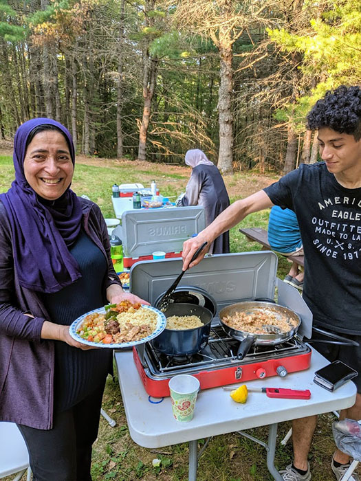 Two people cooking food on a campstove.