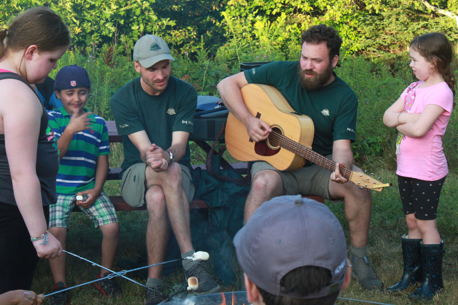 Participants roast marshmallows and sing songs at a campfire.