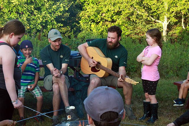 Learn-to camp staff and participants roast marshmallows and sing songs at a campfire.