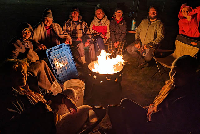A group sits around a campfire at night.