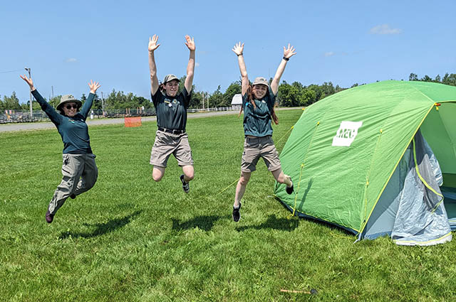 Three staff members jump next to a tent.
