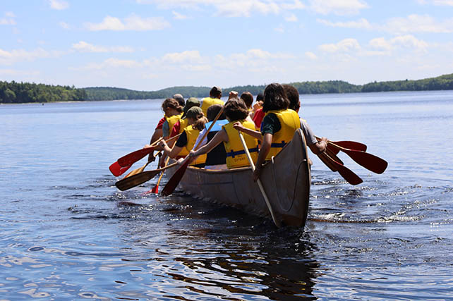 A group of people wearing life jackets in a big canoe.