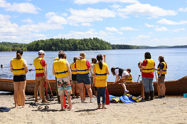 A group of people wearing life jackets ready to get into a big canoe.
