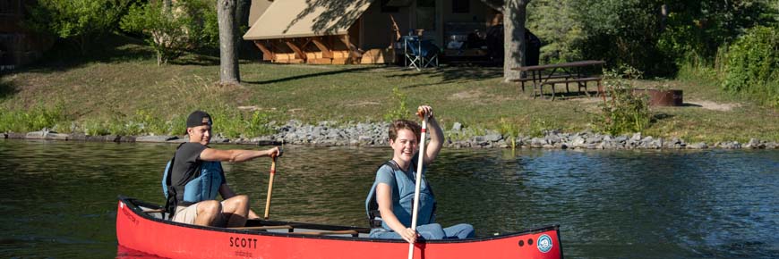 Two visitors canoeing with an oTENTik tent in the background.