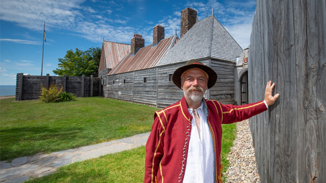 A costumed interpreter stands in front of the Habitation.