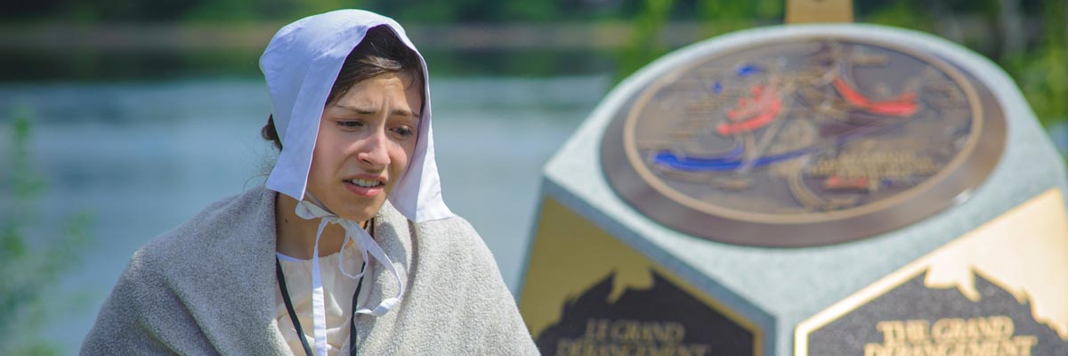 A woman in period costume in front of the Grand Derangement monument.