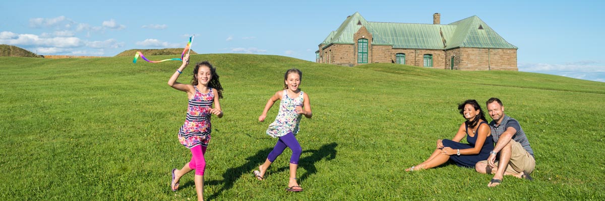 Deux jeunes filles, sous le regard de leurs parents, courent sur un vaste terrain gazonné.