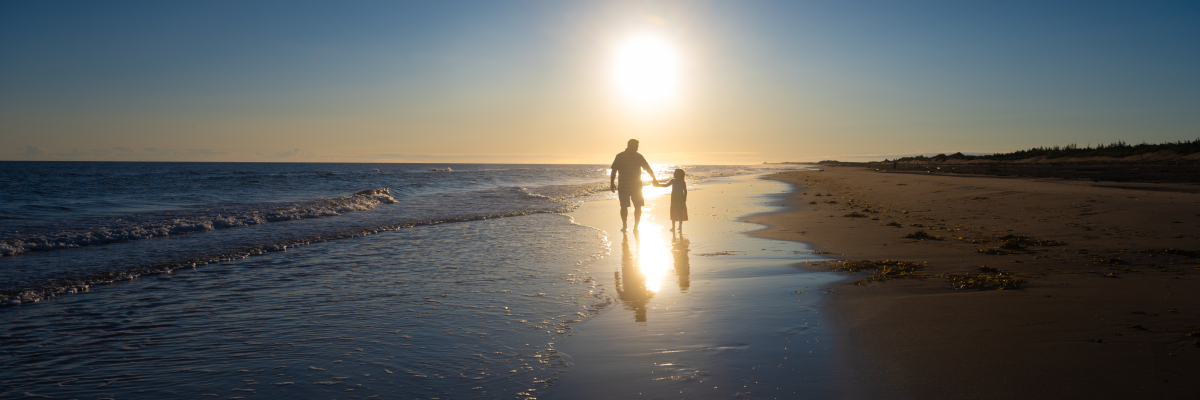 Un adulte et un enfant sur la plage de Brackley avec le soleil en arrière-plan au parc national de l’Île-du-Prince-Édouard.