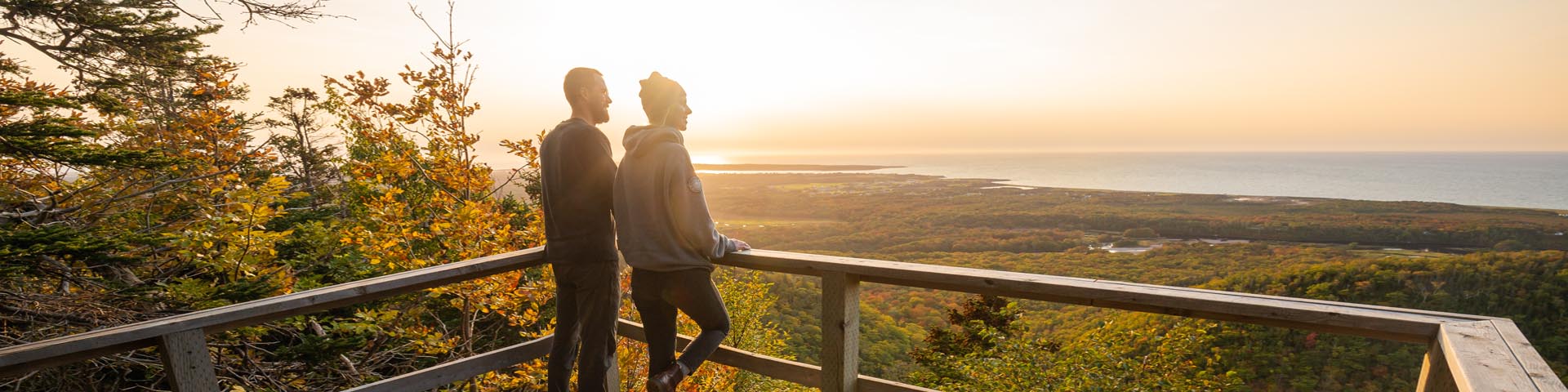 Two visitors on a lookout are looking at the forest and the sea, in Cape Breton Highlands National Park.