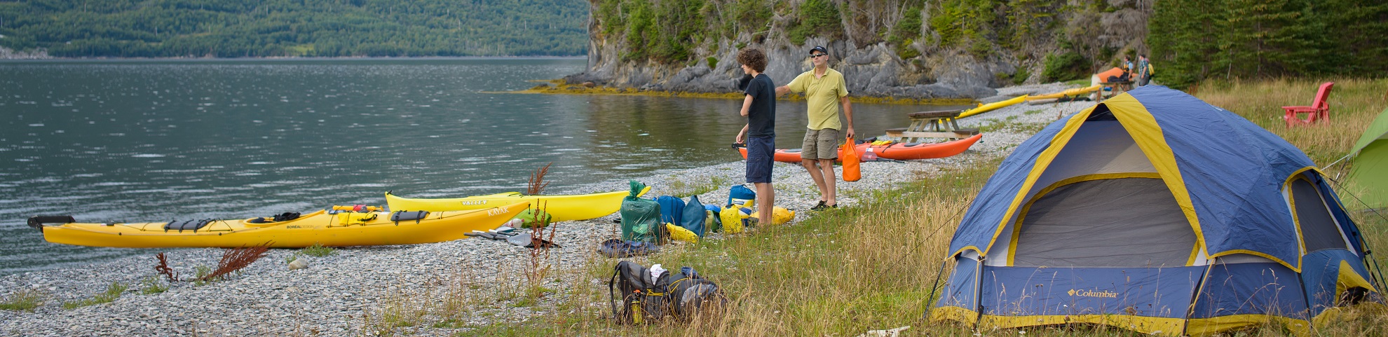 Des tentes, des kayaks et des gens sur une plage isolée dans un fjord au parc national du Gros-Morne.