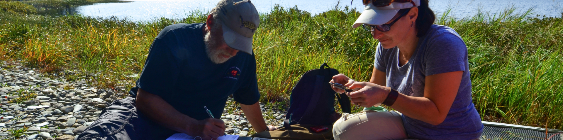 Two people doing field work on a lake shore.