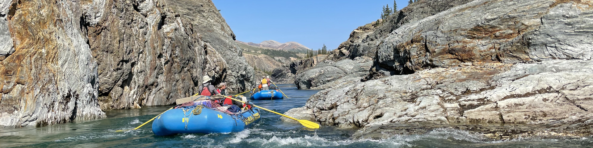 Deux groupes de personnes font du rafting en eau vive dans un ravin.
