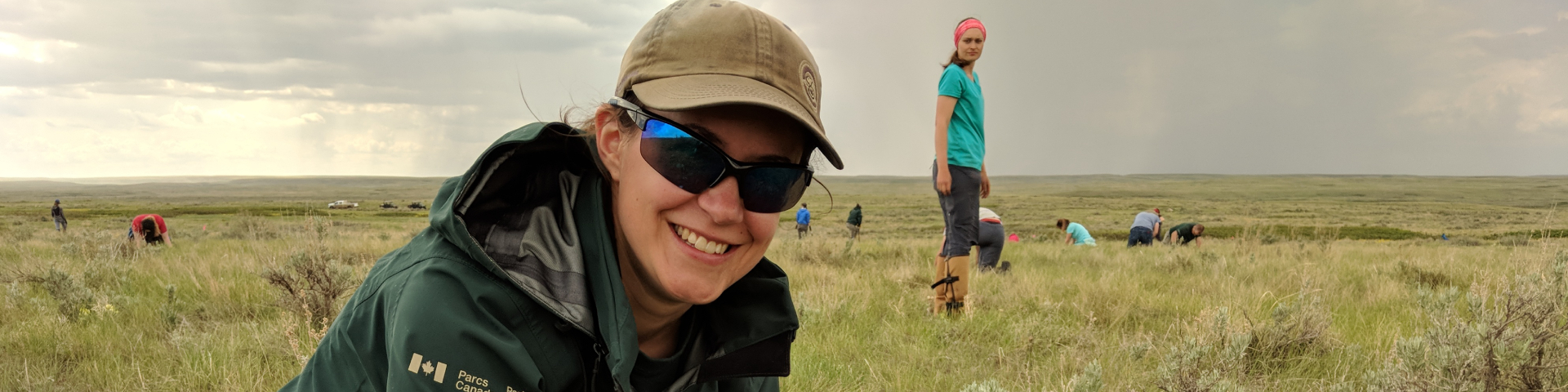 A Parks Canada employee and a group of volunteers doing field work in a prairie landscape.