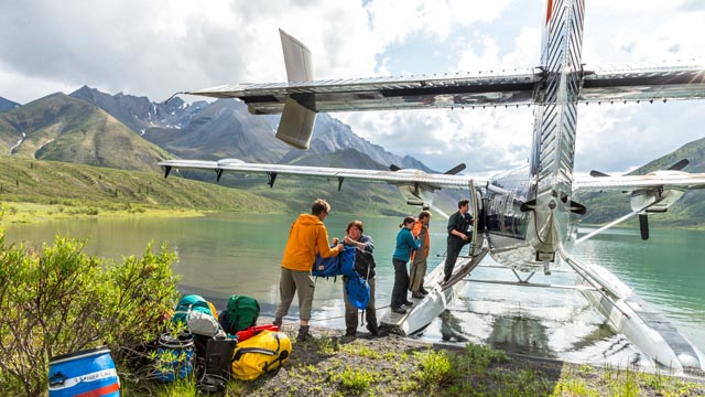 Cinq adultes déchargeant du matériel de camping de l'hydravion au lac Grizzly Bear, dans la réserve de parc national Nááts'ihch'oh.