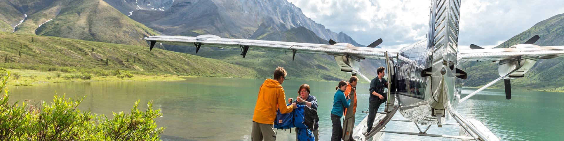 Five adults unloading camping gear from the float plane at Grizzly Bear Lake, in Nááts’ihch’oh National Park Reserve.