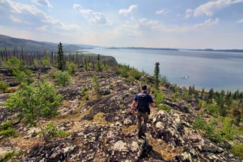A man hikes with a scenic view of the lake in Thaidene Nene National Park Reserve.