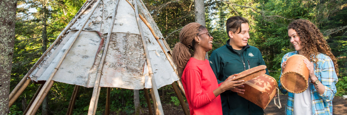 Visiteurs en compagnie d’un guide du parc découvrant les paniers en écorce de bouleau au camp anishinaabe.