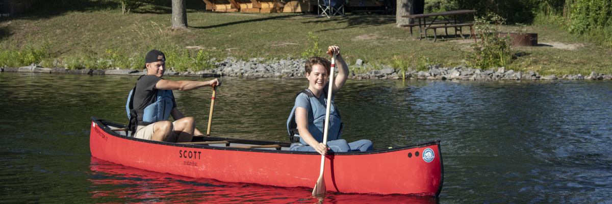 Deux visiteurs en canot, avec une tente oTENTik en arrière-plan.