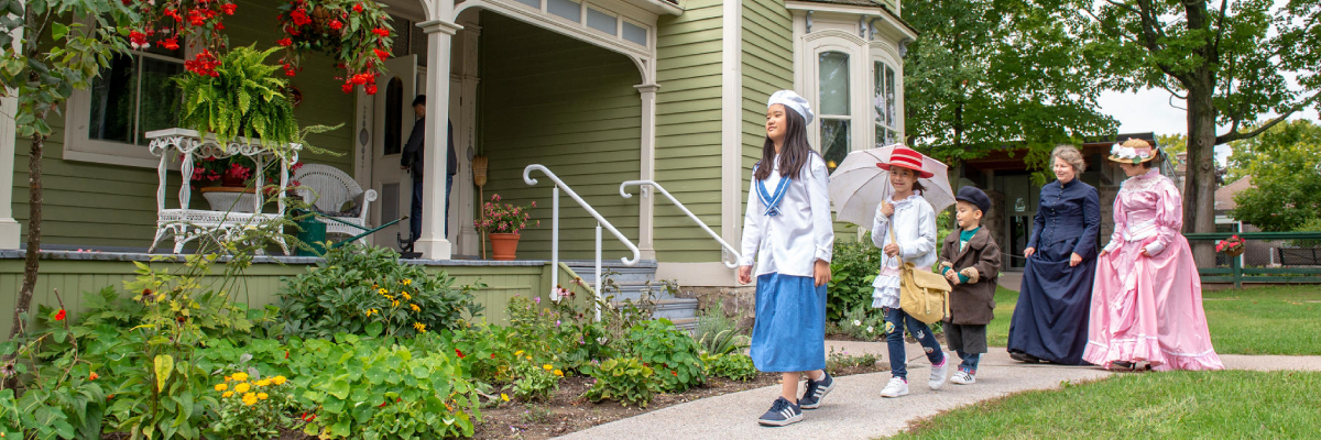 A guide and visitors in period costumes walking in front of the Victorian home at the Bethune Memorial House National Historic Site.