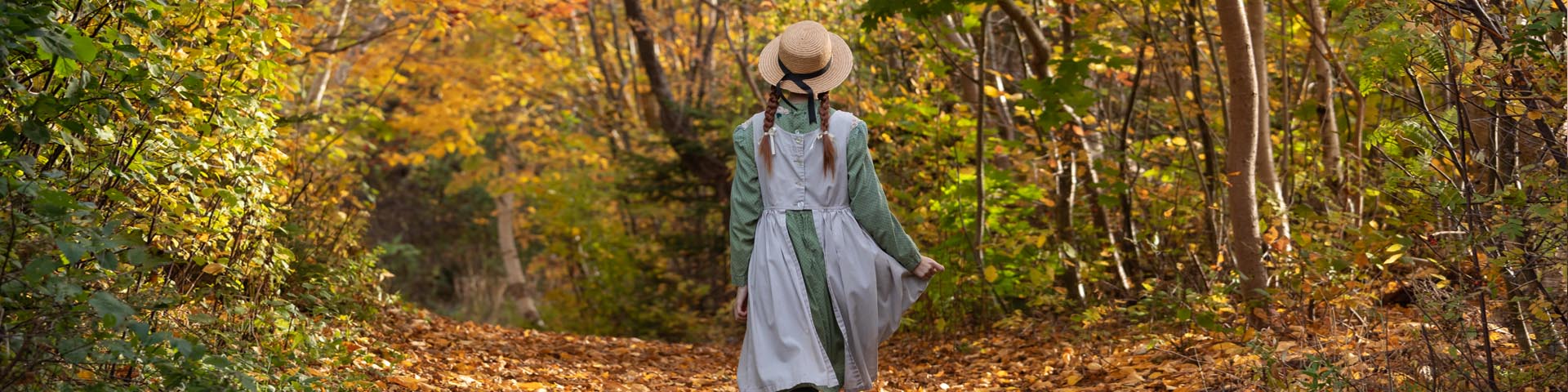 A young woman dressed as the fictional character Anne Shirley walks down a dirt laneway in the fall.