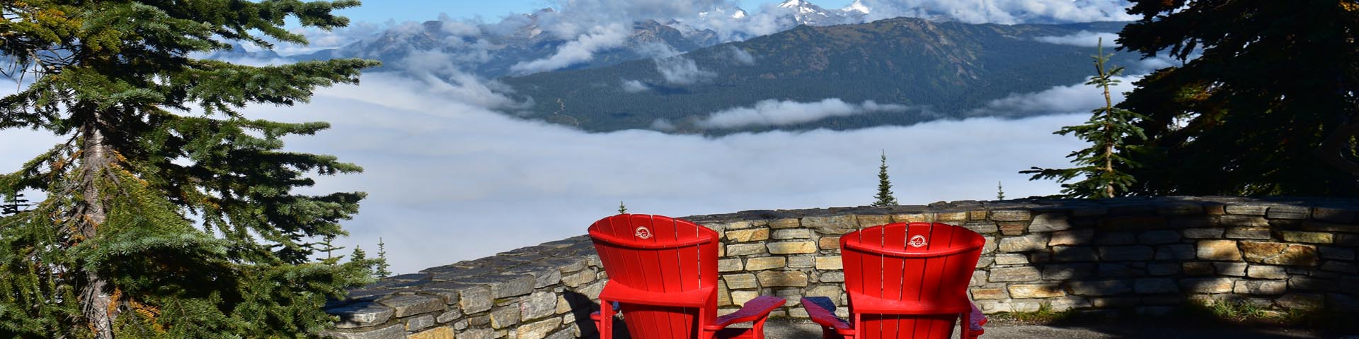 Two red chairs sit behind a stone wall at a mountain viewpoint