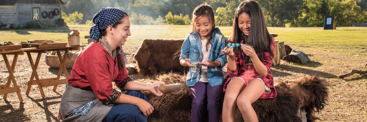 Young visitors learn about beadwork with the help of a costumed animator at the Indigenous encampment.