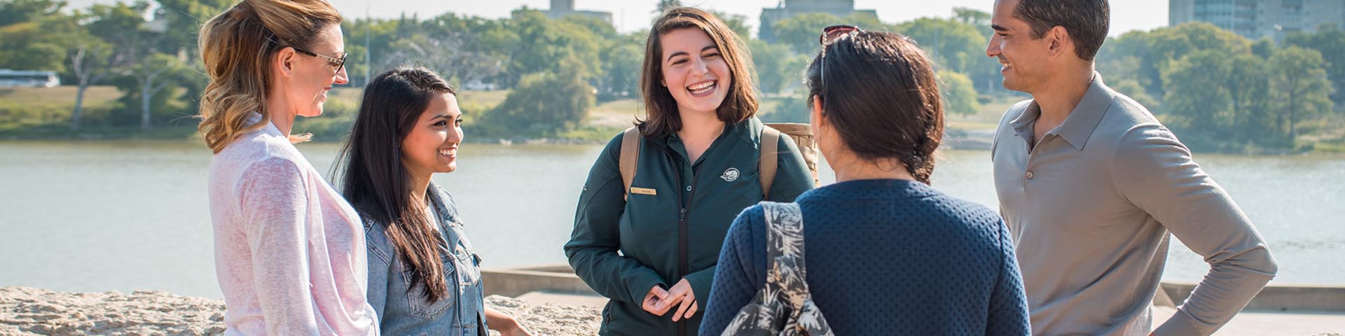 A Parks Canada employee talking to 4 visitors on the waterfront at The Forks National Historic Site.