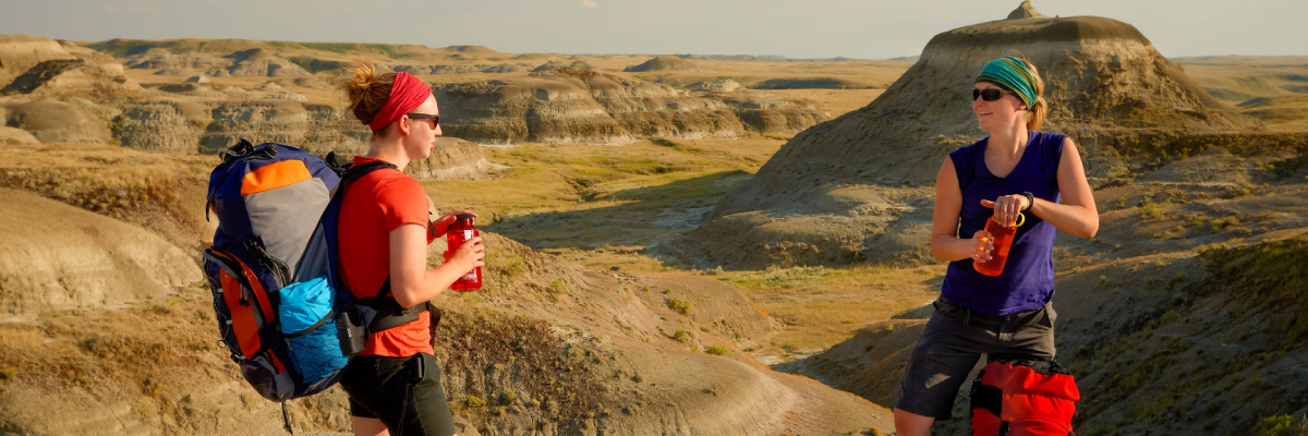 Two young women take a break and drink water during their hike on Valley of 1000 Devils Trail. 