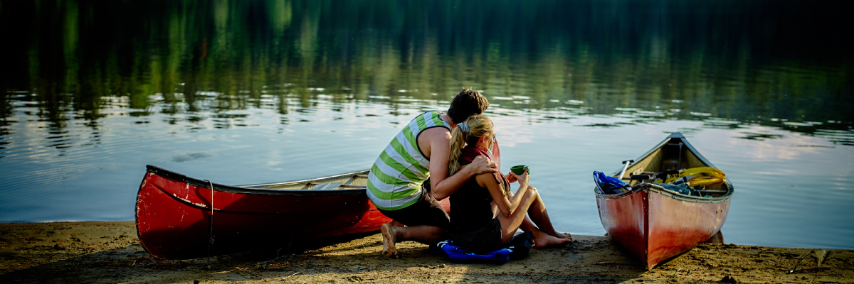 A couple is sitting by the lake near canoes.