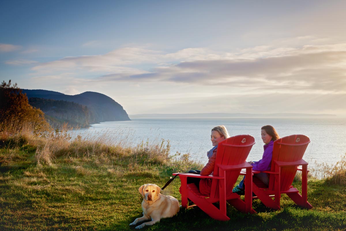 Deux femmes assisent sur une chaise rouge, lors d'un coucher de soleil, dans la Baie de Fundy.