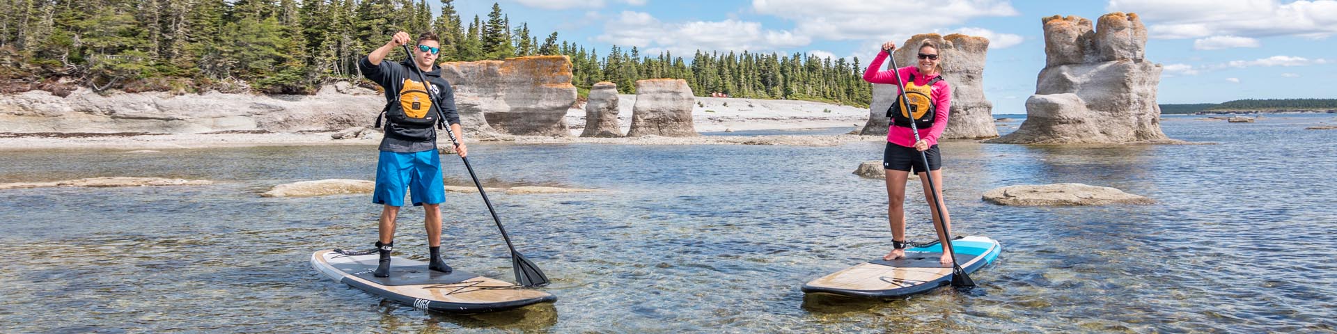 A young couple paddleboarding in Anse aux érosions, south of Île Quarry, on a sunny day. 