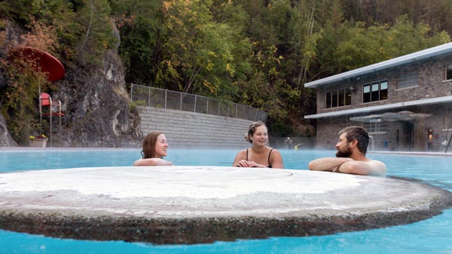 Three friends enjoying a fall soak in the hot pool. Trees on the rockwall surrounding the pool are slowly changing colour. 