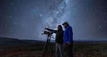 Deux personnes sur une plate-forme en bois avec un télescope et un ciel étoilé dans le parc national des Hautes-Terres du Cap-Breton.