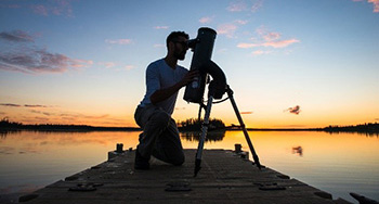 A visitor uses a telescope at dusk on the dock at Astotin Lake