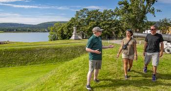 Standing on top of the earthworks at Fort Anne National Historic Site, a Parks Canada interpreter gives a tour of the site to two summer visitors.