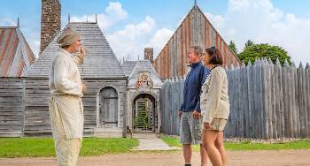 Standing by the entrance at Port-Royal National Historic Site a Parks Canada interpreter gives a tour of the site to two summer visitors. 