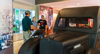 A Parks Canada staff member speaks with visitors near a historic mobile blood transfusion vehicle inside a visitor centre.