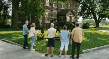 Group of visitors and an interpreter standing in front of the Administration Building at the Sault Ste. Marie Canal National Historic Site. 